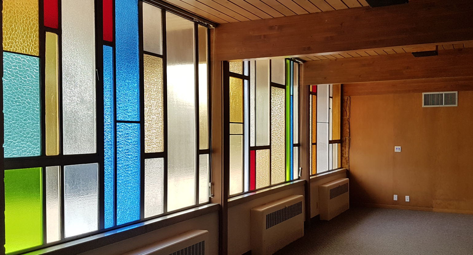 Photo of a room with colorful translucent glass windows; wooden beams, walls, and ceiling; and heating vents
