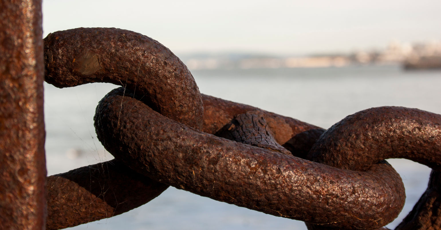Photo of large rusty iron chain with blurry sea in background