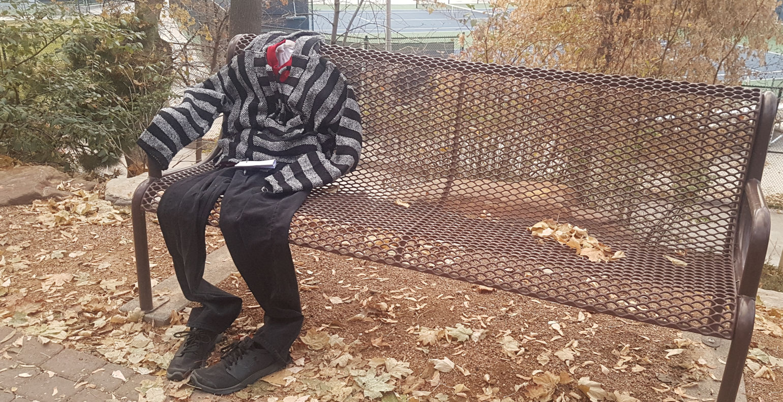 Empty clothes in the shape of a human sitting on a bench with fall leaves