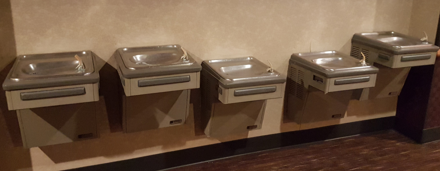 5 drinking fountains mounted on a wall at varying levels