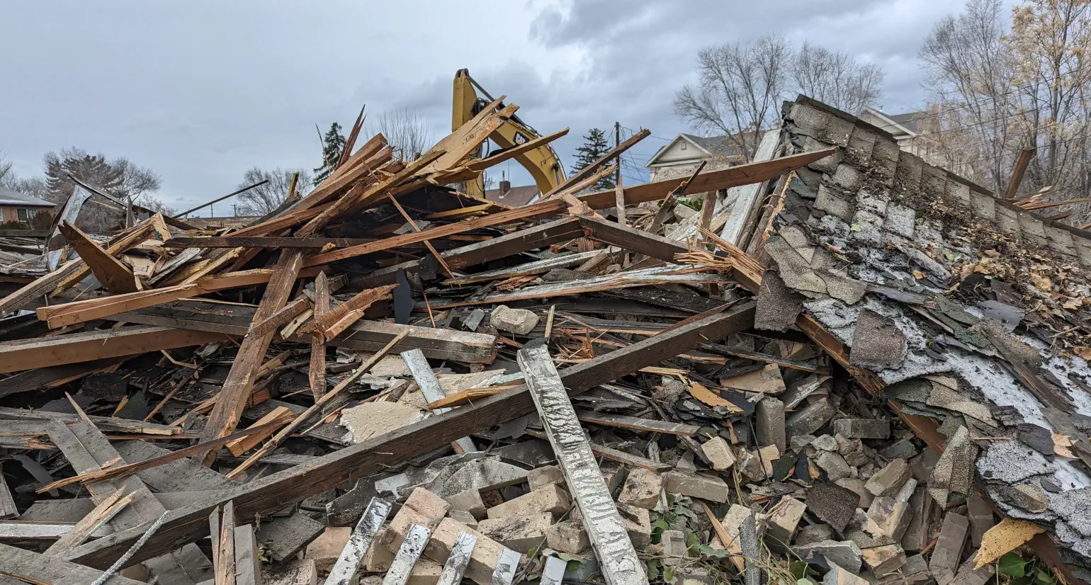 Rubble of a demolished house in front of a guilty-looking Caterpillar excavator