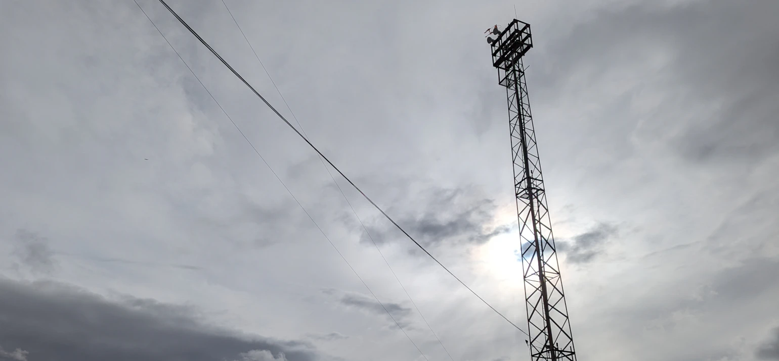 Metal tower with cables in front of overcast sky and muted sun
