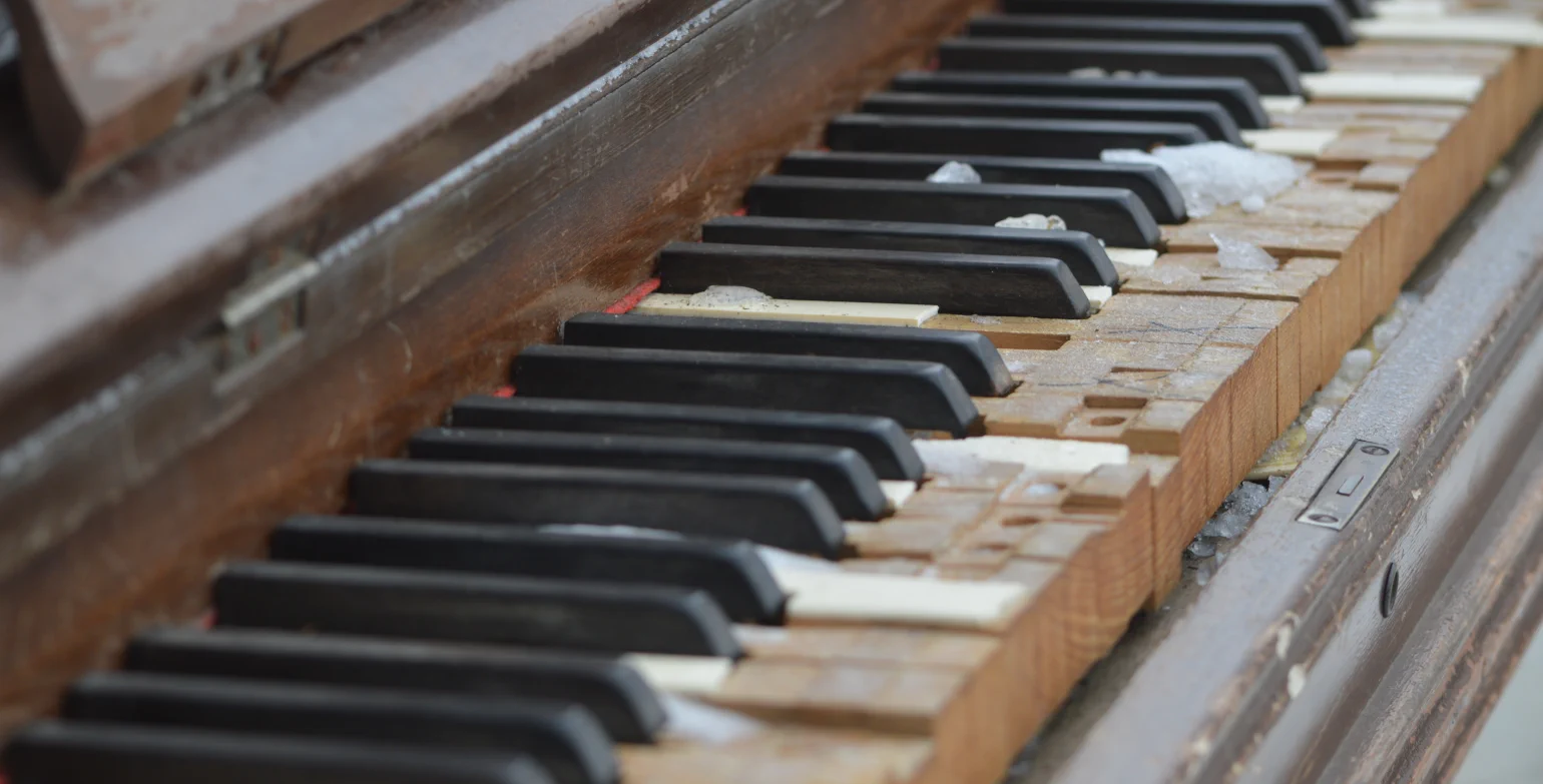 Old piano outdoors, focused on keyboard with most keytops missing and some snow on it