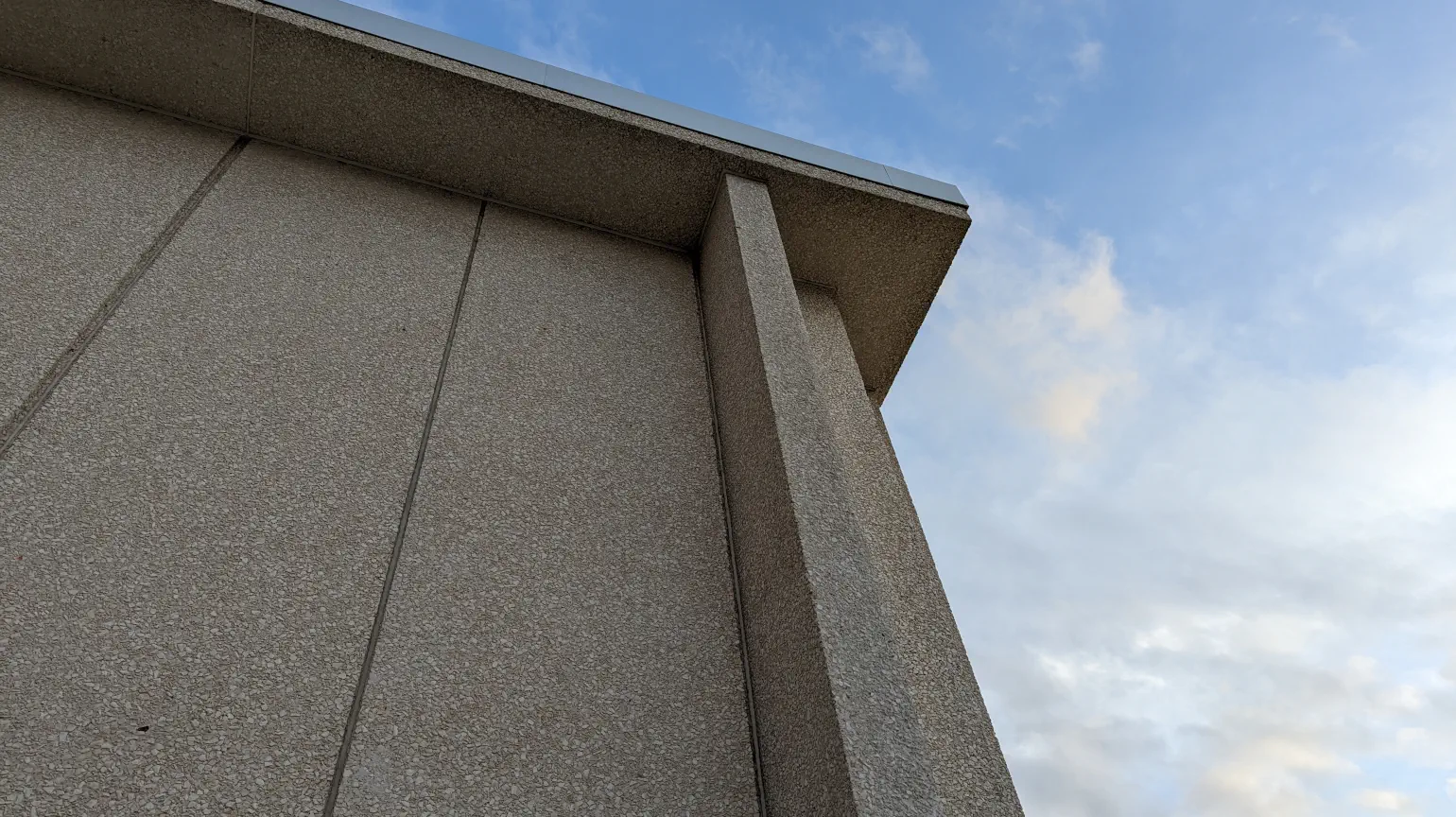 Photo looking from ground level up at concrete and crushed stone building against a blue sky with some white clouds