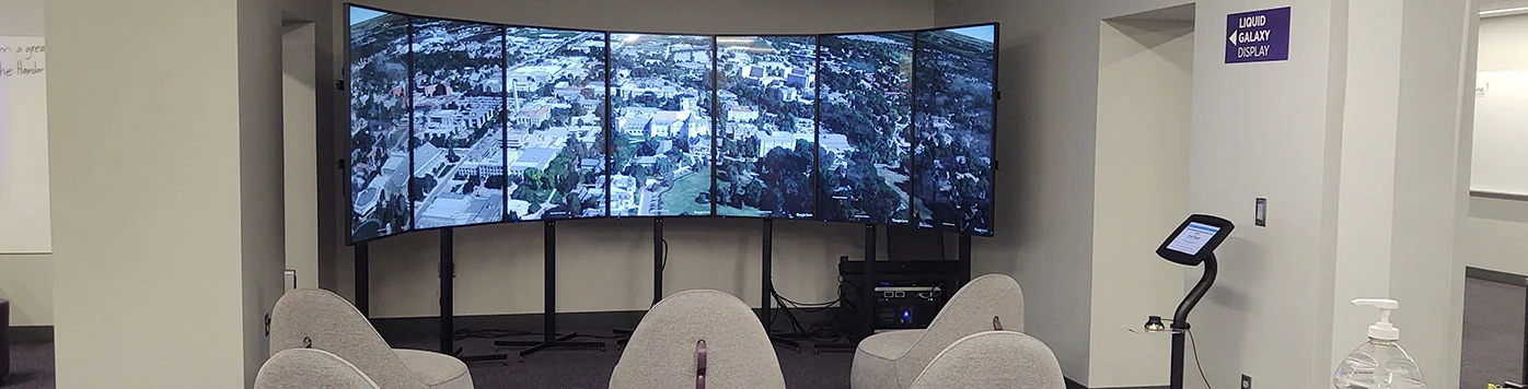 A photo of Kansas State University’s VisionPort in its library. Several modern chairs are set up facing the 7-screen VisionPort, displaying KSU’s campus on Google Earth.
