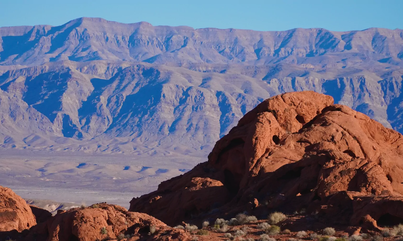 Weathered red rocks jut out from the desert into the foreground, while a blue haze covers a mountain range in the background.