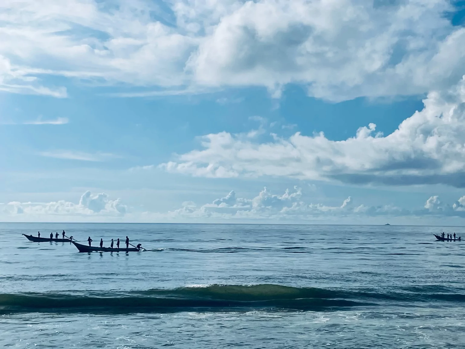 The sun has just started to rise over the horizon. A group of fishermen can be seen pushing their small wooden boats into the water, preparing to start their day’s work. The air is still cool and quiet, with only the sound of waves gently lapping against the shore as the fishermen row out into the open sea, ready to begin their early morning fishing expedition.