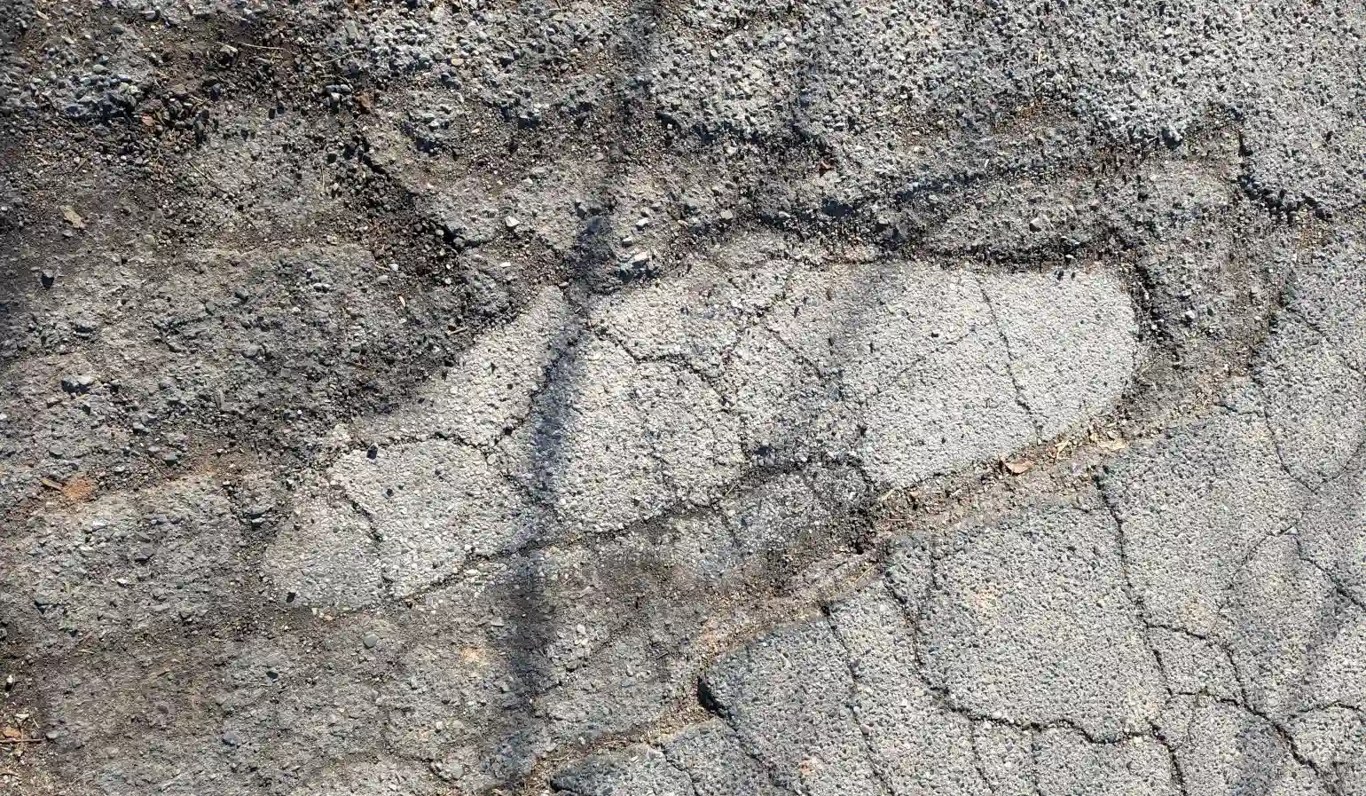 Photograph of several layers of blacktop road with cracks and shadows