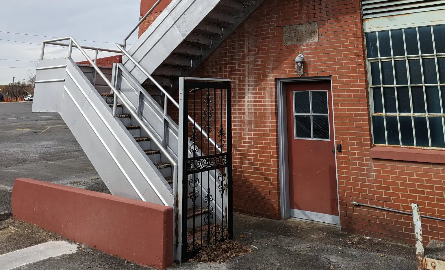 Photograph of brick building fronted by a metal staircase leading to the roof, gated by a full-size metal door that would be trivially easy to climb around