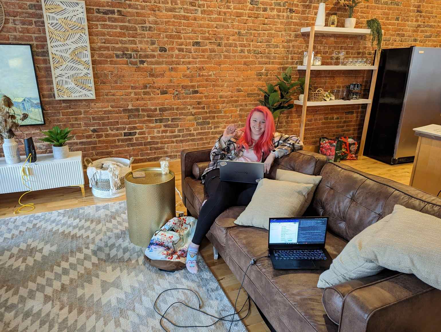 Casablanca. A spacious lounge room with an exposed brick wall, with part of the kitchen visible in the top right. A grey patterned rug sits on the floor. An End Pointer sits on a leather couch with her laptop. Another laptop sits on the couch.