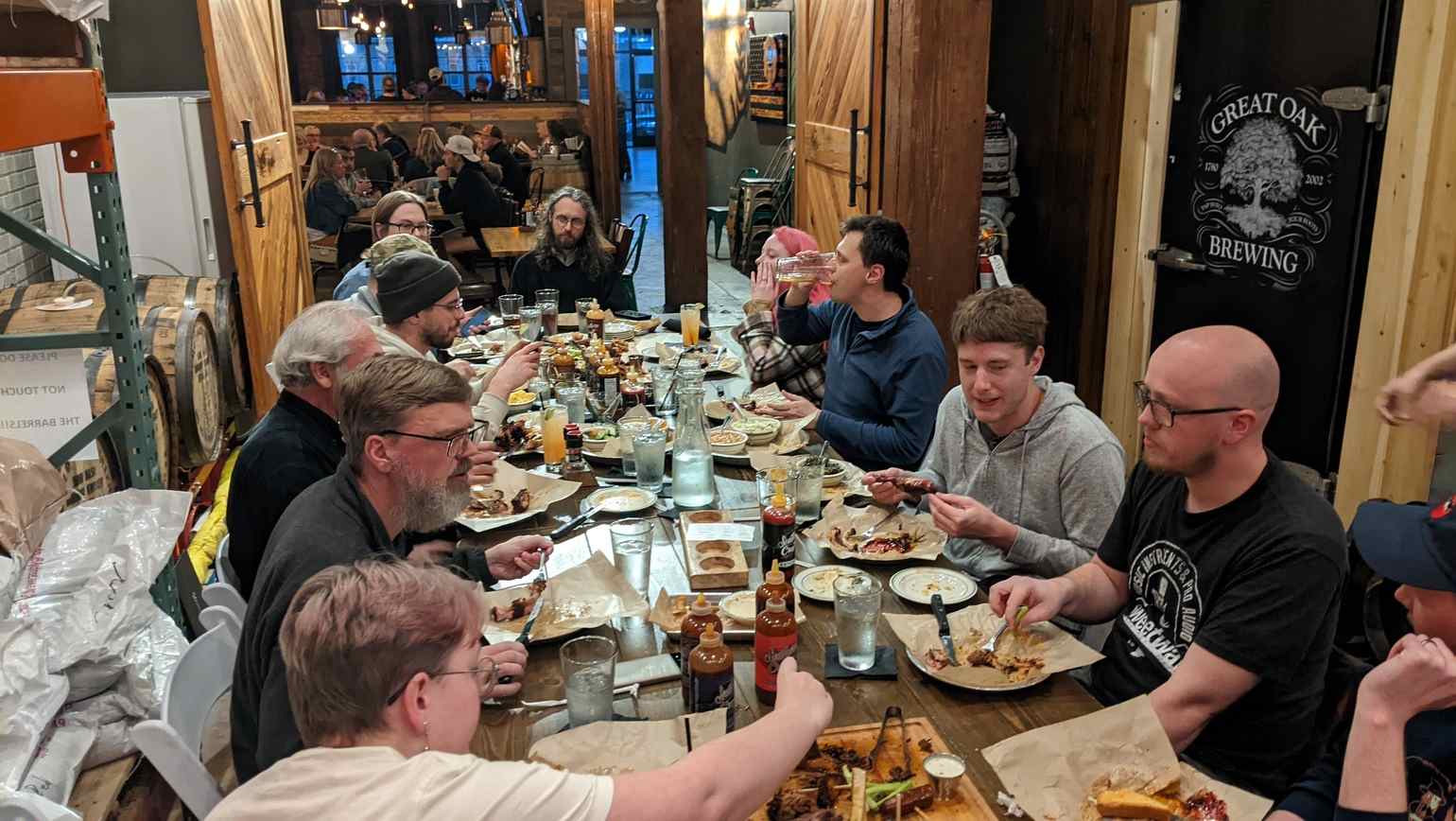 Dinner. End Pointers are gathered around a large restaurant table, with lots of hearty food in front of them, midway through the meal. A sign in the background reads “Great Oak Brewing”.