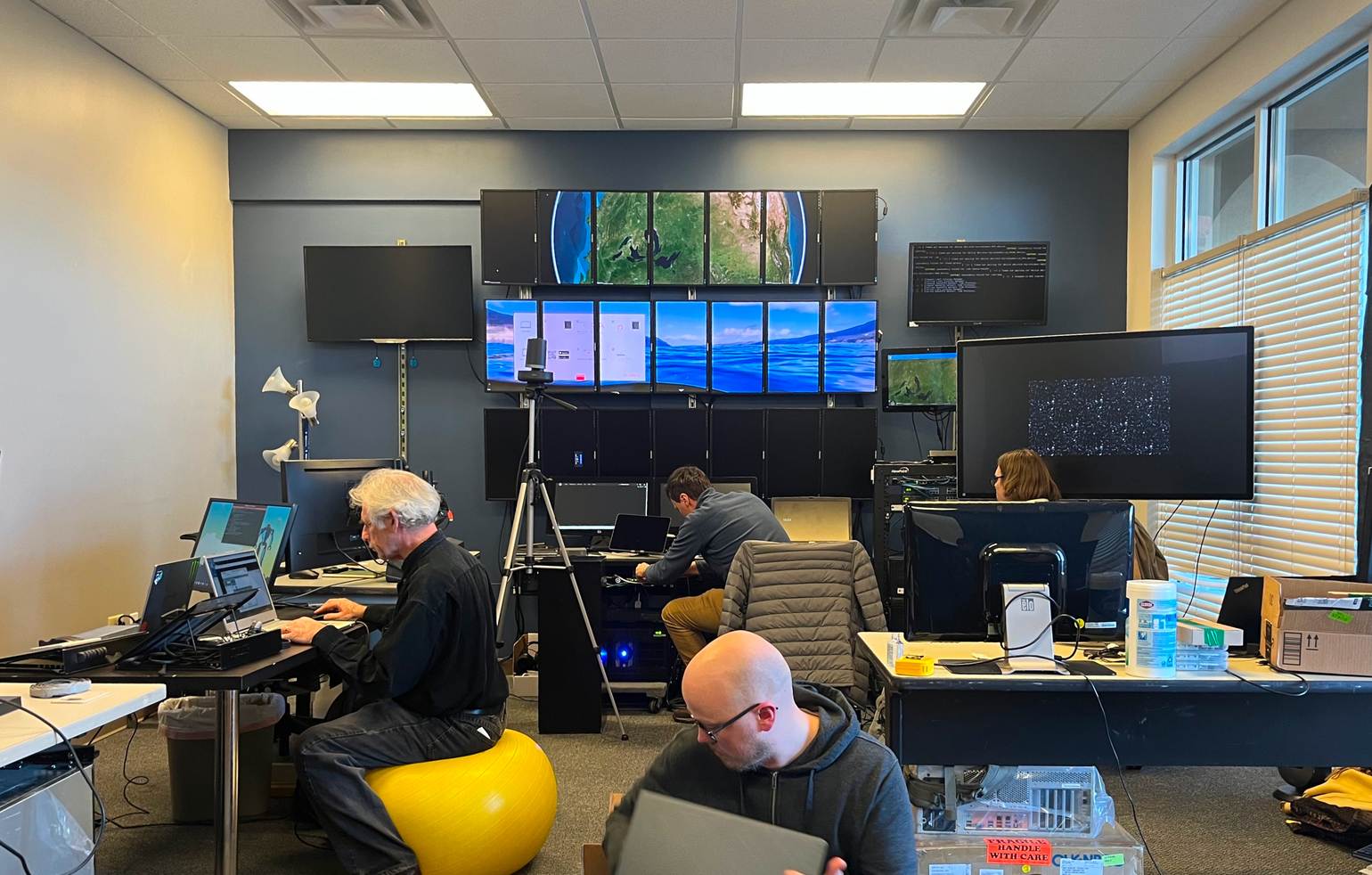 EPTN main room. Several development VisionPort systems are mounted on the back wall. Four End Pointers are seen sitting at a variety of desks and workstations.