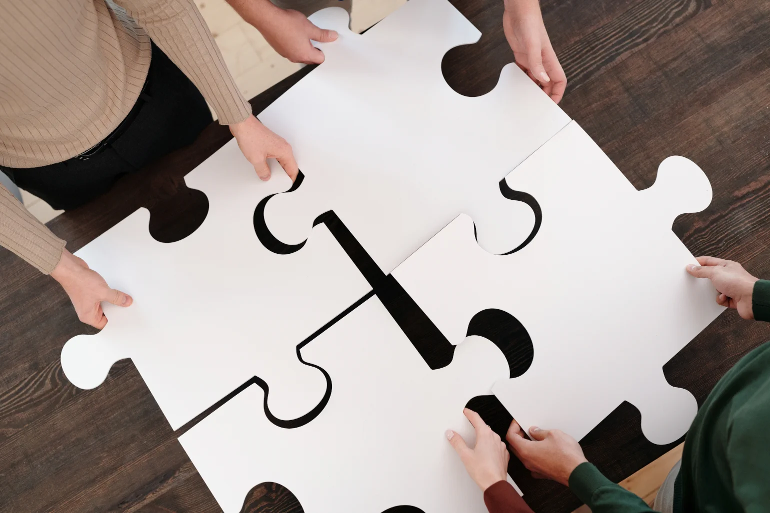 Overhead view of 4 people standing on opposite sides of a table holding huge puzzle pieces