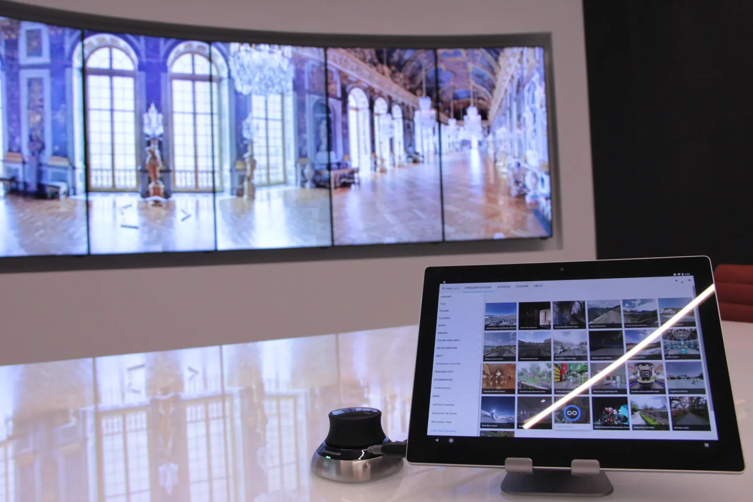 A 3D mouse and a tablet sit on a reflective white table, in front of a VisionPort 7-screen array enclosed in a nice white cabinet. On the screen is displayed a 360-degree panorama of a museum.