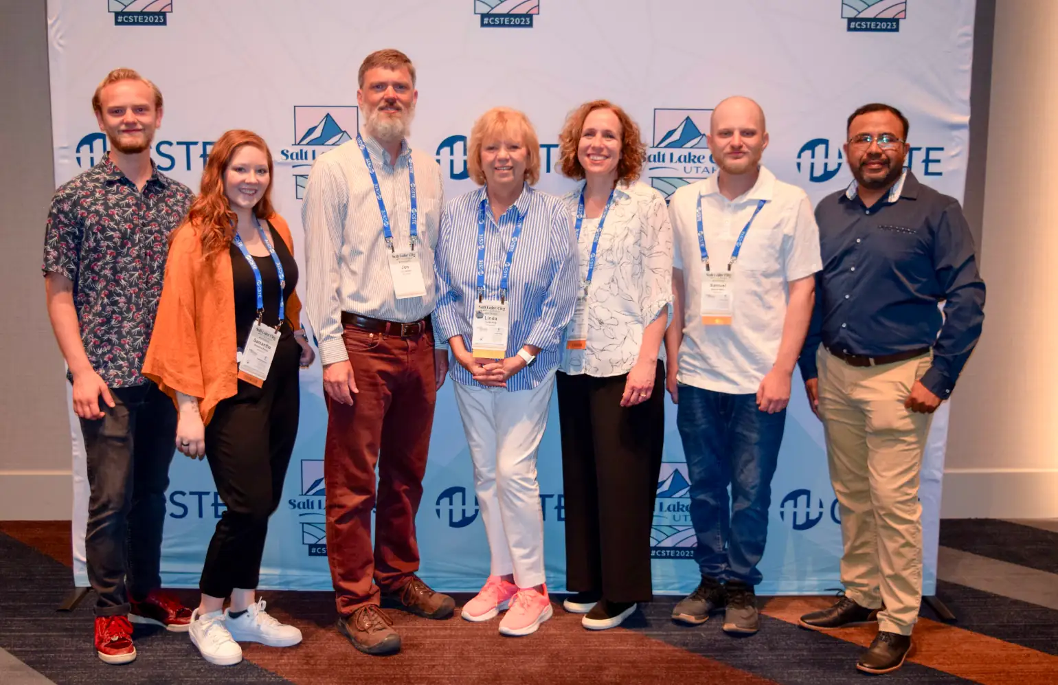 Seven members of the End Point CasePointer team standing in front of the CSTE 2023 press wall