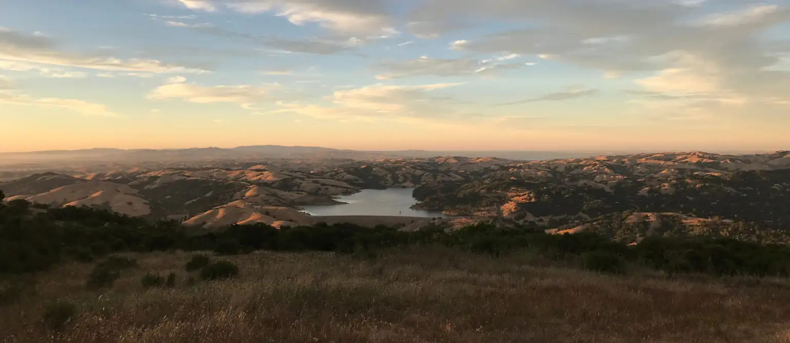 Looking east from the top of the Berkeley hills over the Briones Reservoir. Rolling hills are seen in the distance with the sun setting to the west.