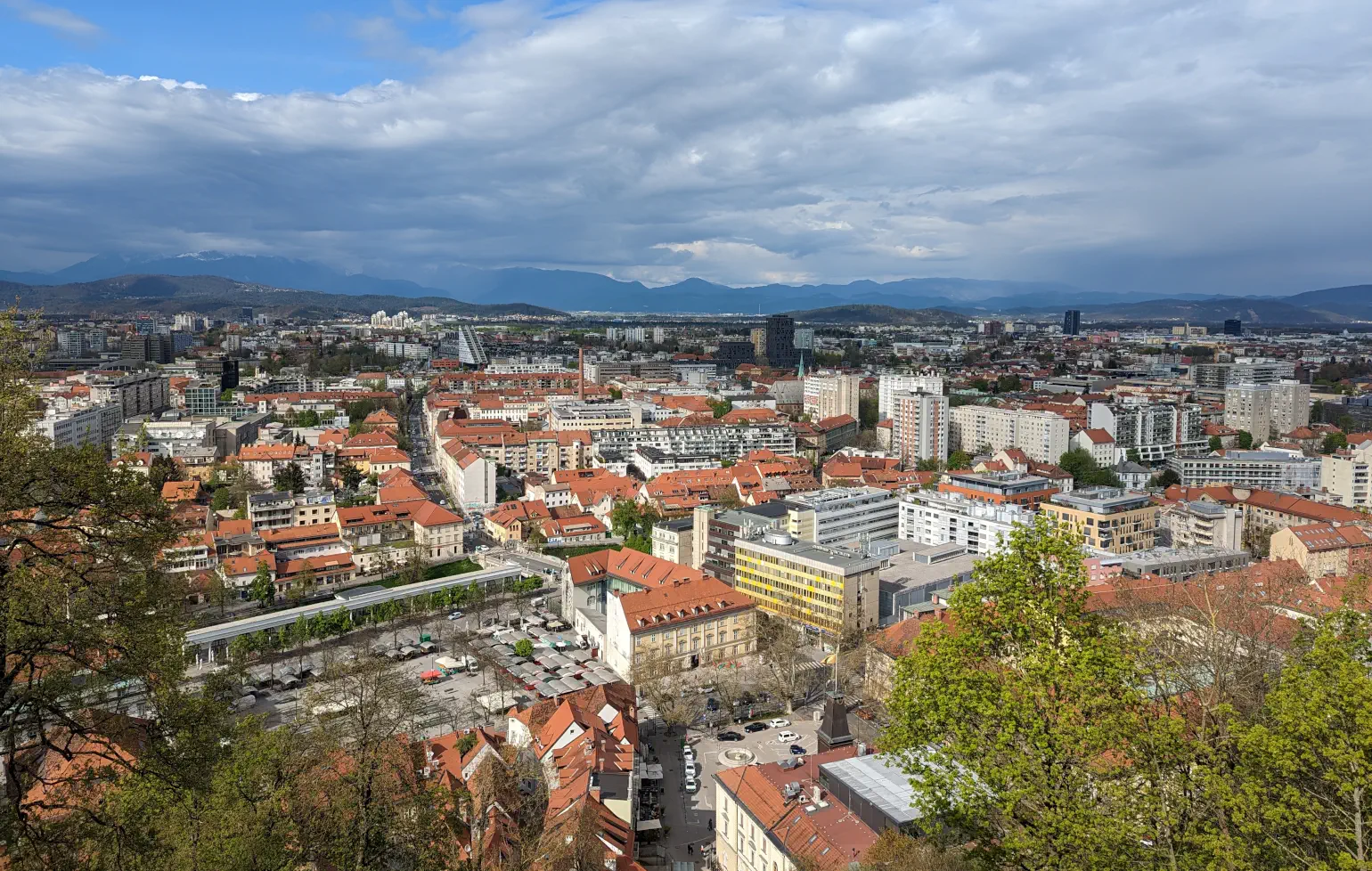 A sunny view overlooking a European city with classic and modern architecture, with mountains in the background