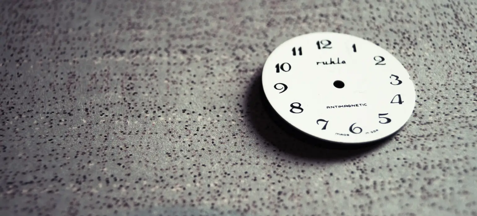 A white watchface, without any other parts, sits on a surface with a dotted texture