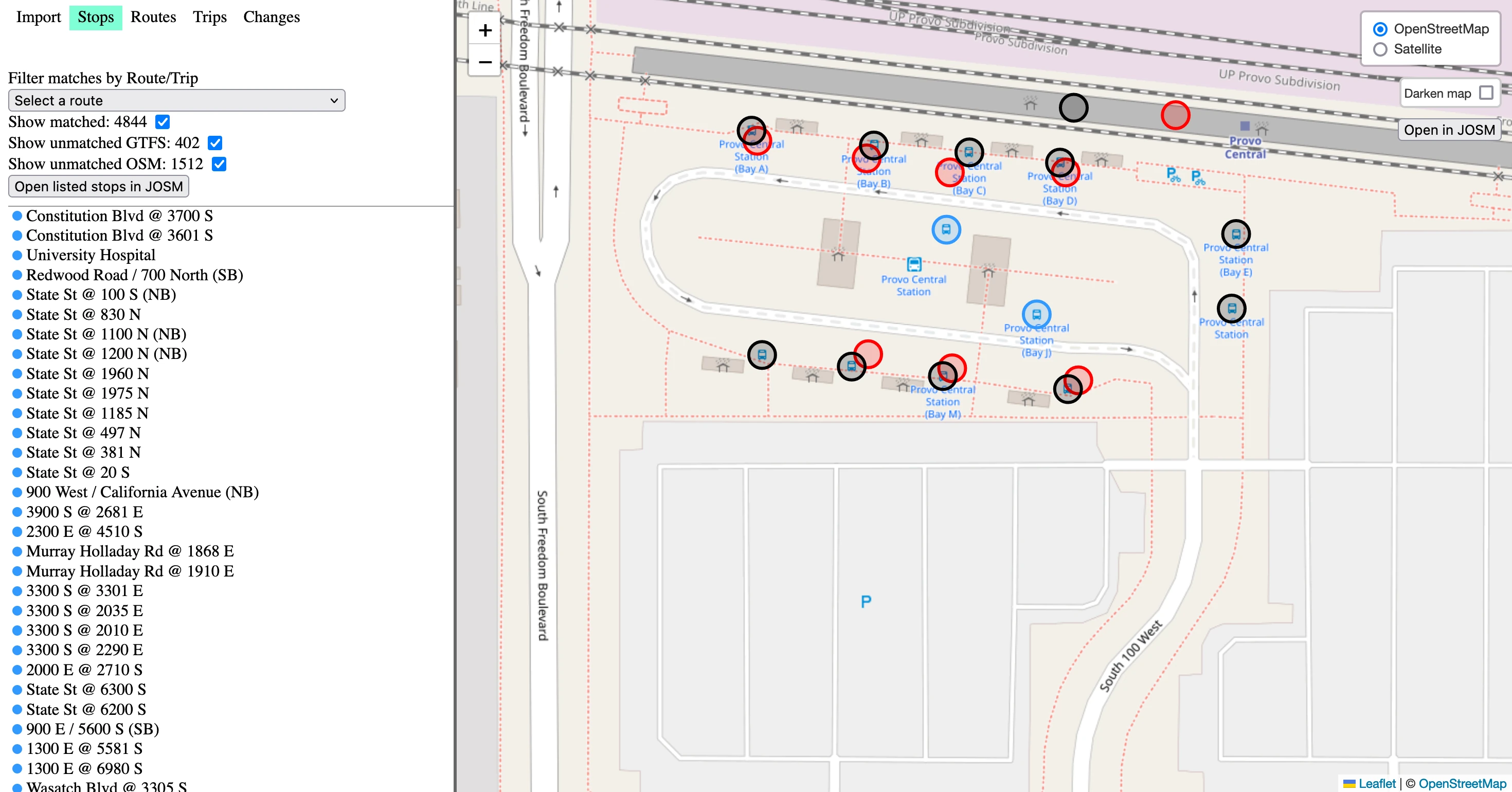 The OSM editing app. The “Stops” navigation option is selected. On the map, there are black dots on top of bus stops visible in the actual map texture. Most of these black dots have nearby red circles. There are a couple of blue dots on top of bus stops. The text in the left app bar reads: “Filter matches by Route/Trip” then a dropdown select box reading “Select a route”. Then, “Show matched: 4844” with a checked checkbox. Then, “Show unmatched GTFS: 402” with a checked checkbox. Then, “Show unmatched OSM: 1512” with a checked checkbox. Then a button, “Open listed stops in JOSM”. Then, a list of bus stops: “Constitution Blvd @ 3700 S” with a blue circle, “Constitution Blvd @ 3601 S” with a blue circle, etc.