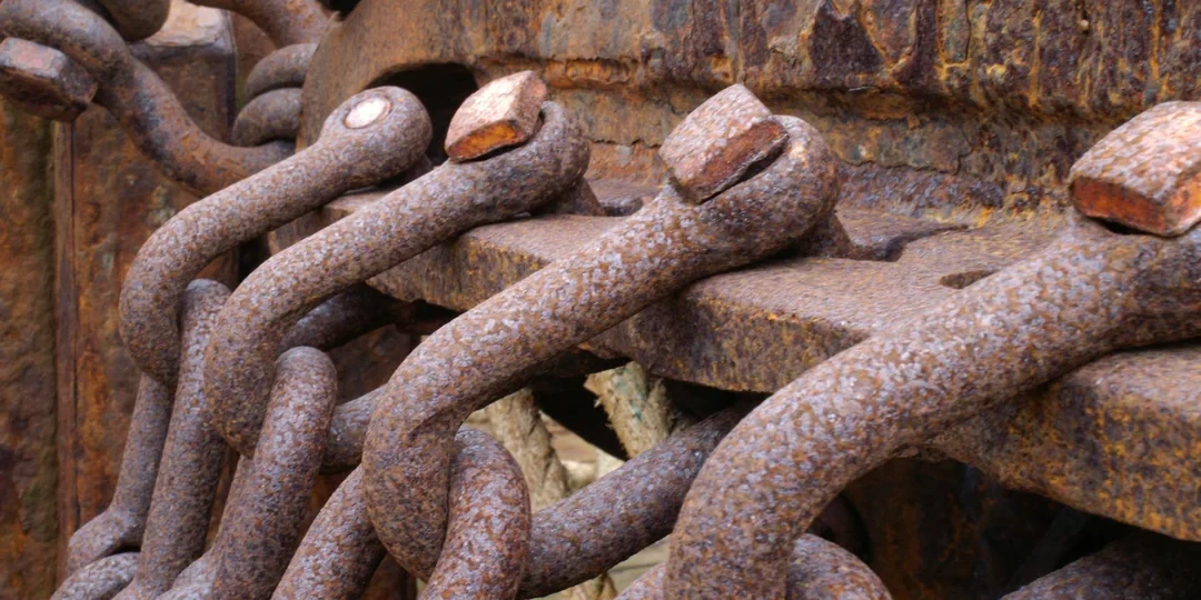 Several rusty chains are tied into the side of a rusty metal structure.