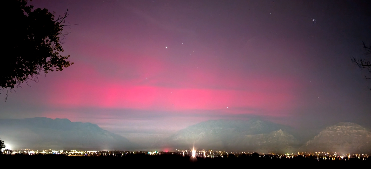The northern lights glow red above a mountain valley filled with city lights