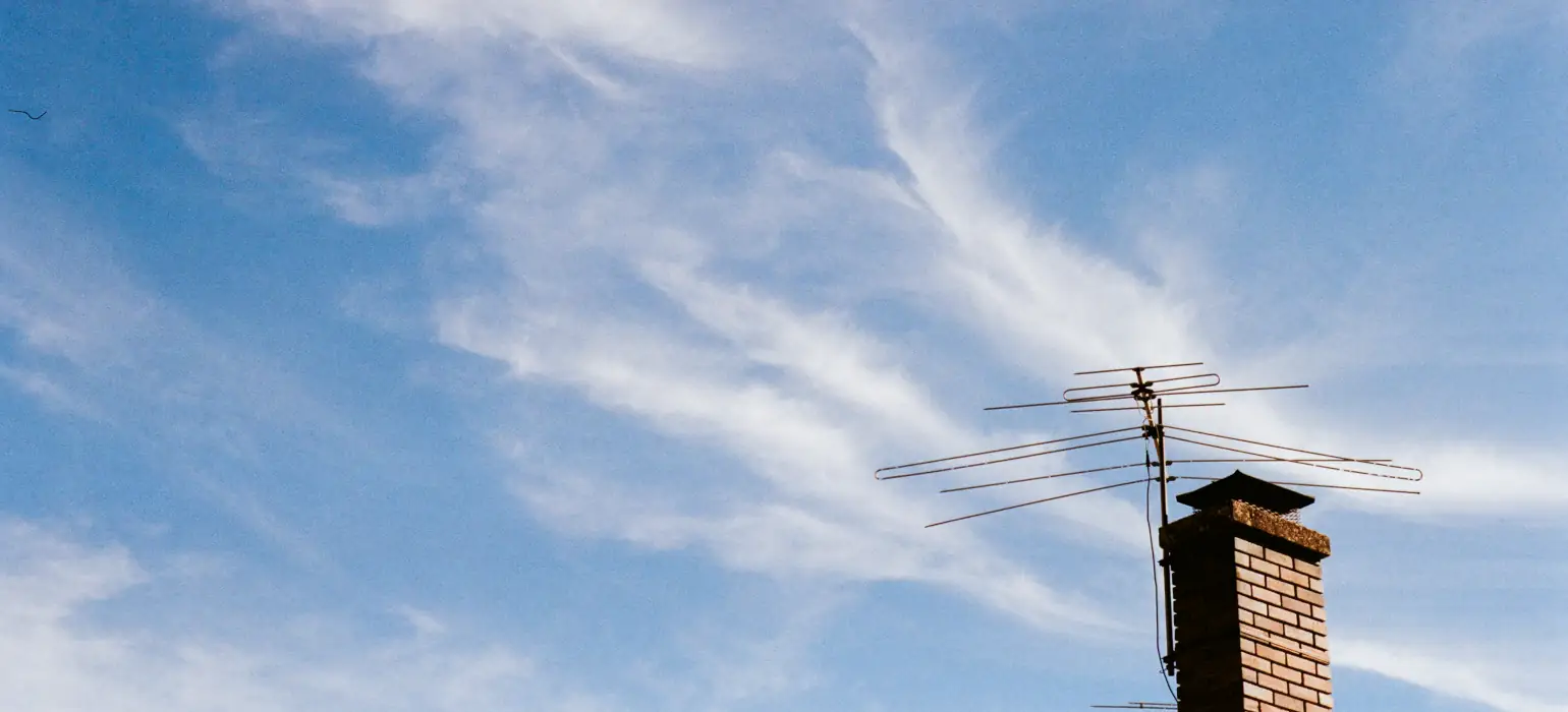 Against a blue sky with wispy white clouds, an old directional antenna points to the left of the camera atop a brick fireplace
