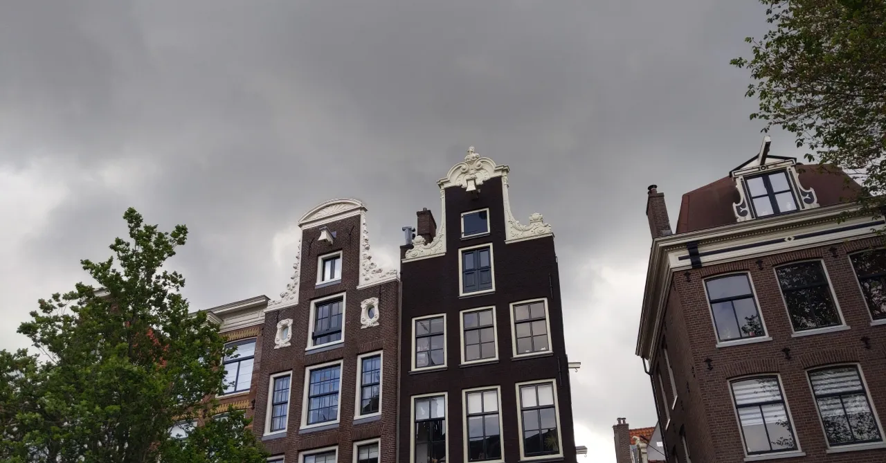 Traditional Dutch canal houses with ornate gabled facades photographed from below against a stormy sky.